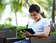 smiling man looking at tablet while sitting outside under trees