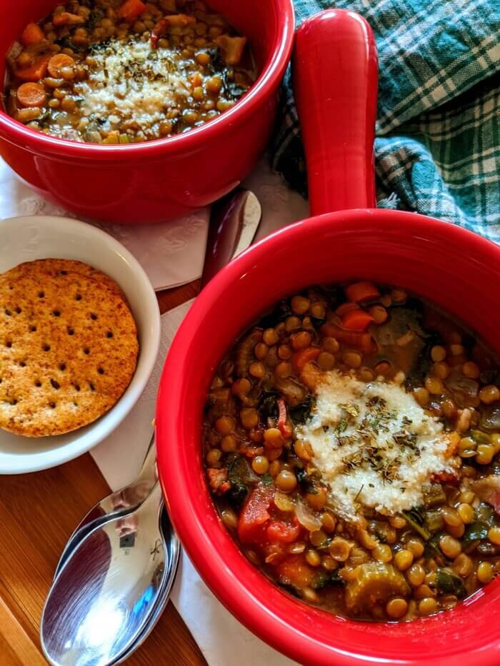two red bowls of lentil stew with a white bowl of crackers and silver spoons
