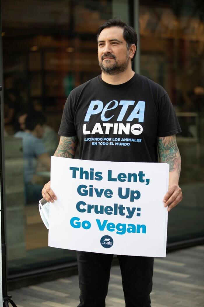 Man wearing black with a serious expression and holding a sign asking people to go vegan for Lent