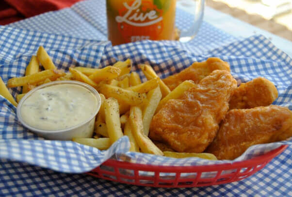 vegan battered fish with French fries and vegan tartar sauce in blue and white checked paper and red plastic basket