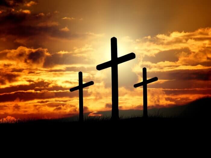 three crosses in dark shadow silhouette against backdrop of red and orange sunset